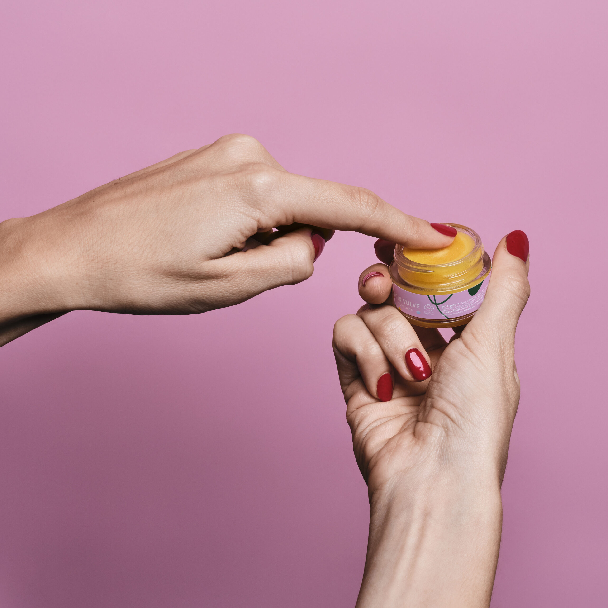 Mains de femme en train de tenir le baume Goliate et d'en appliquer sur son doigt.